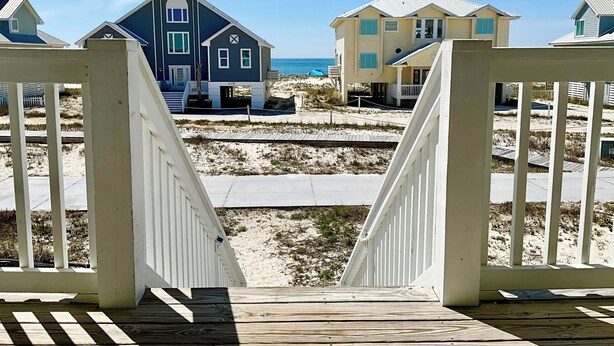 A wooden deck leading to a beachfront property with two houses, one blue and one yellow, and a sandy beach in the background. - Easy Beach Access & Pools!  Morgantown (Gulf Shores)