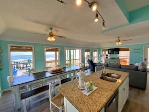 A spacious kitchen with a central island, dining area with chairs, and a view to the outside.