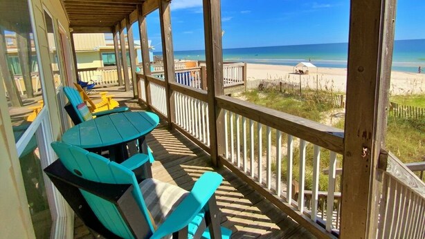 A covered outdoor area with a wooden deck, blue chairs, and a view of the beach. - Beach Front & Pet Friendly (Gulf Shores)