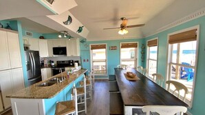 A kitchen with a central island, white cabinets, and a dining area with a long table and chairs. - Beach Front & Pet Friendly (Gulf Shores)