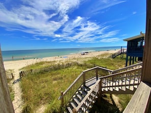 A beach view with a wooden staircase leading to a beach area, a lifeguard tower, and a clear blue sky.