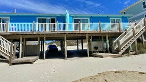 A beachfront property with a two-story building, wooden deck, and a covered area with a grill. - Beachfront & Dog Friendly! (Gulf Shores)