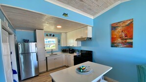 A kitchen with white cabinets, a stainless steel refrigerator, a microwave, and a stove. There is a window with a view of a house and a painting of a sailboat on the wall. - Beachfront in Fort Morgan - Dogs OK (Gulf Shores)