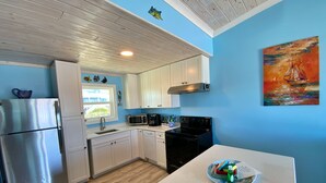 A kitchen with white cabinets, a stainless steel refrigerator, a microwave, and a stove. There is a window with a view of greenery outside. - Beachfront in Fort Morgan - Dogs OK (Gulf Shores)