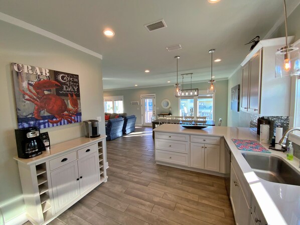 A modern kitchen with white cabinetry, a large island, and a dining area with a view to the outside.