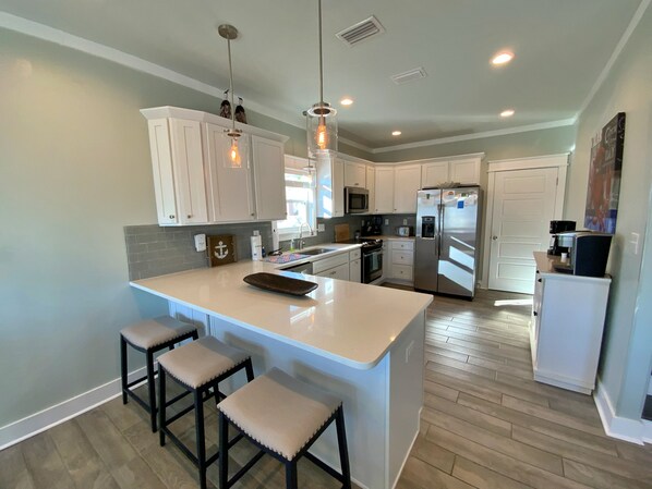 A modern kitchen with white cabinets, a central island with stools, stainless steel appliances, and pendant lighting.