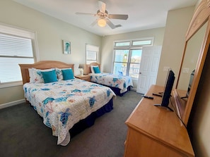 A bedroom with two beds, a ceiling fan, a TV, and a door leading to a balcony.