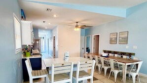 Un coin repas avec une table et des chaises, un ventilateur de plafond et une cuisine en arrière-plan.