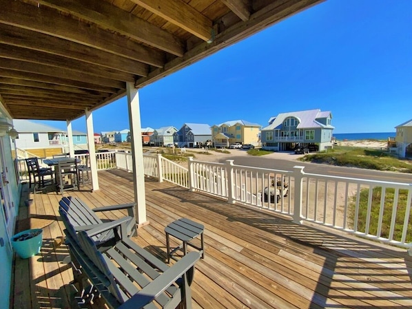 A wooden deck with outdoor seating, a white railing, and houses in the background.