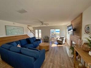 A spacious living room with a blue sectional sofa, a wooden dining table, and a TV mounted on the wall.