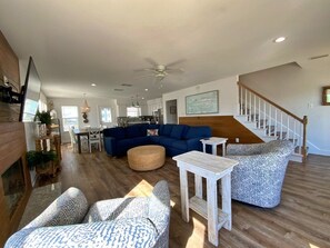 A spacious living room with a blue sofa, patterned armchairs, a coffee table, and a staircase leading to another level.