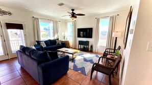 A living room with a dark blue sofa, a coffee table, a TV, and a ceiling fan. - Great Views & Pools! Easy Beach Access (Gulf Shores)