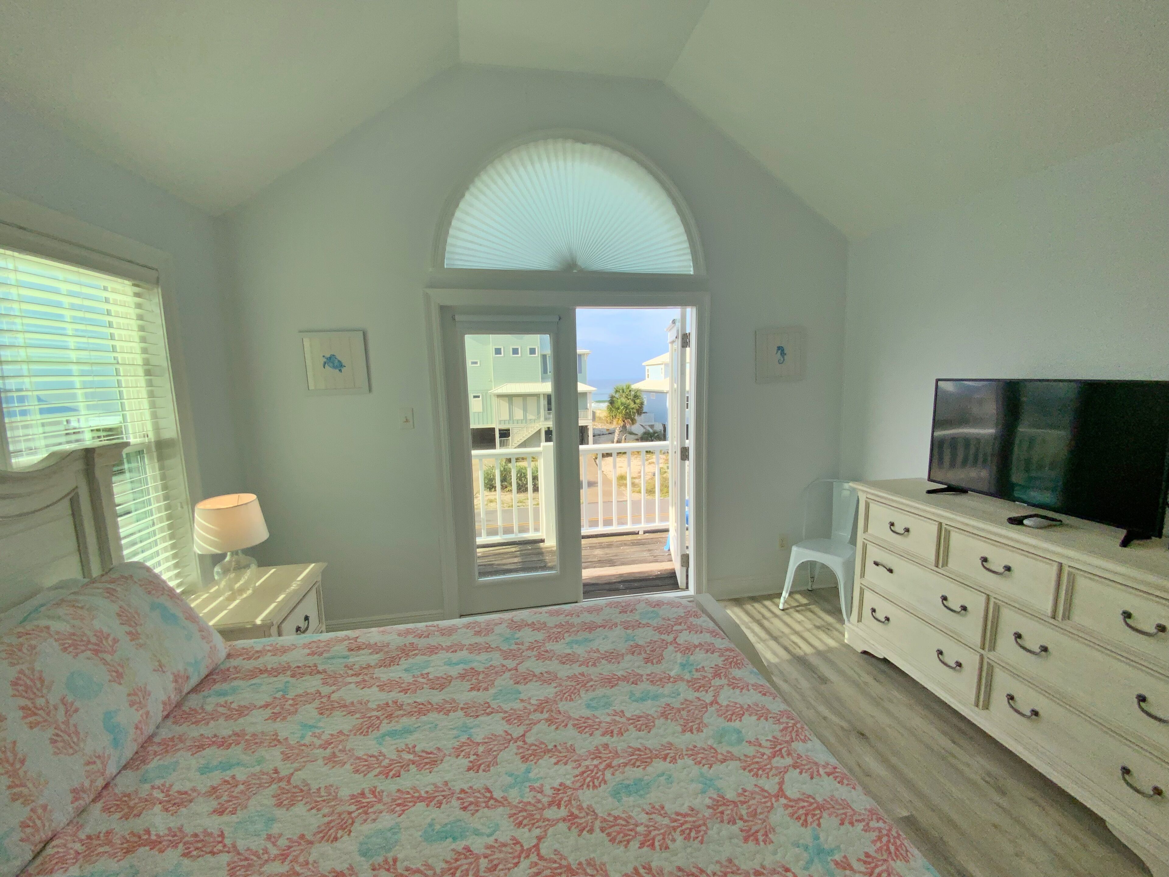 A bedroom with a bed, a TV, a dresser, and a door leading to a balcony.