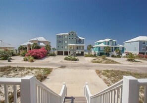 A beachfront residential area with houses, a sandy driveway, and a staircase leading to a gated entrance.