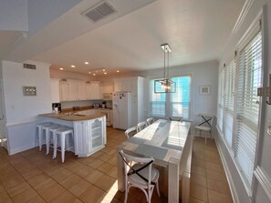 A modern kitchen with white cabinetry, a central island, and a dining area with a long table and chairs.