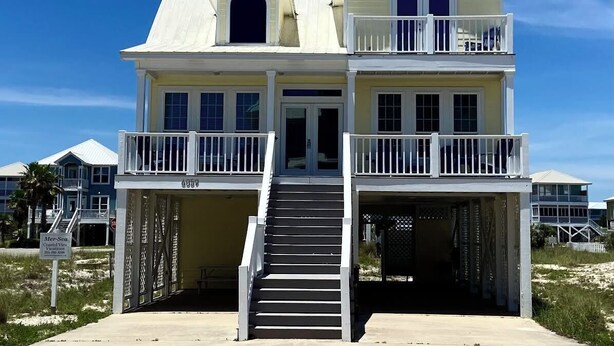 A two-story beach house with a balcony on the upper floor, a covered front porch, and a staircase leading to the entrance. - Great Gulf Views & Pools, Pickleball (Gulf Shores)