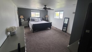 Ein Schlafzimmer mit Bett, Nachttischen, Deckenventilator und Fenstern.
