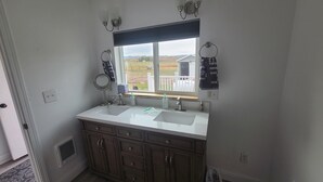 Ein Badezimmer mit einem doppelten Waschbecken, Holzschränken, einem Fenster mit Blick auf ein Haus und einem Handtuchhalter.