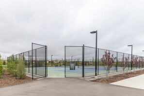 Ein Tennisplatz mit Maschendrahtzaun, einem Schild und einer Straßenlaterne.