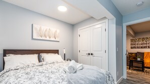 A bedroom with a large bed, a wooden headboard, a white door, and a painting on the wall. - Deluxe Suite w/Fast WiFi, Perfect for Long Stays (Airdrie)