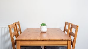 Een houten eettafel met vier stoelen, een witte pot met een groene plant en een witte radiator.