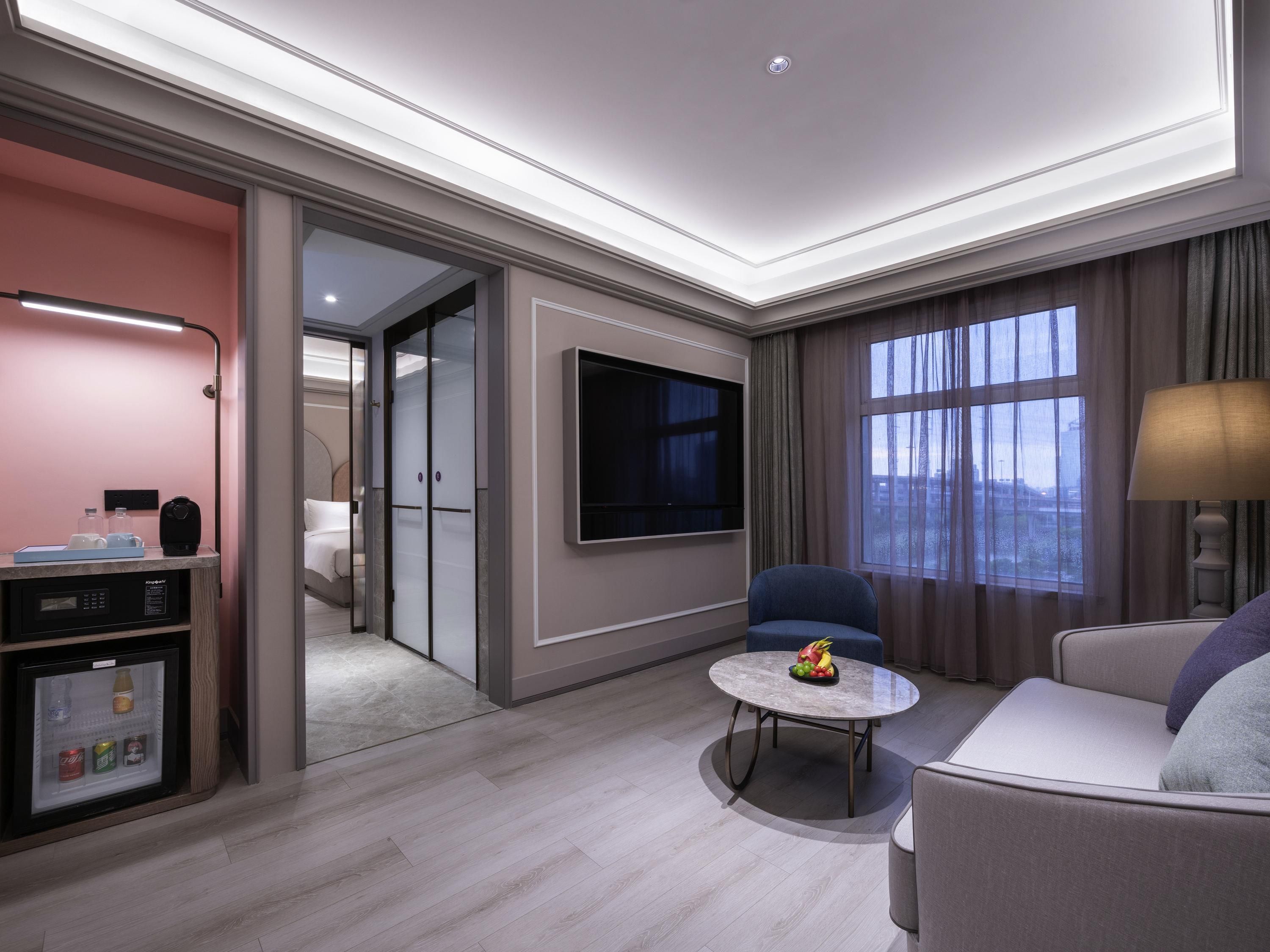 A modern hotel room with a flat-screen TV, a seating area with a round table, and a minibar.