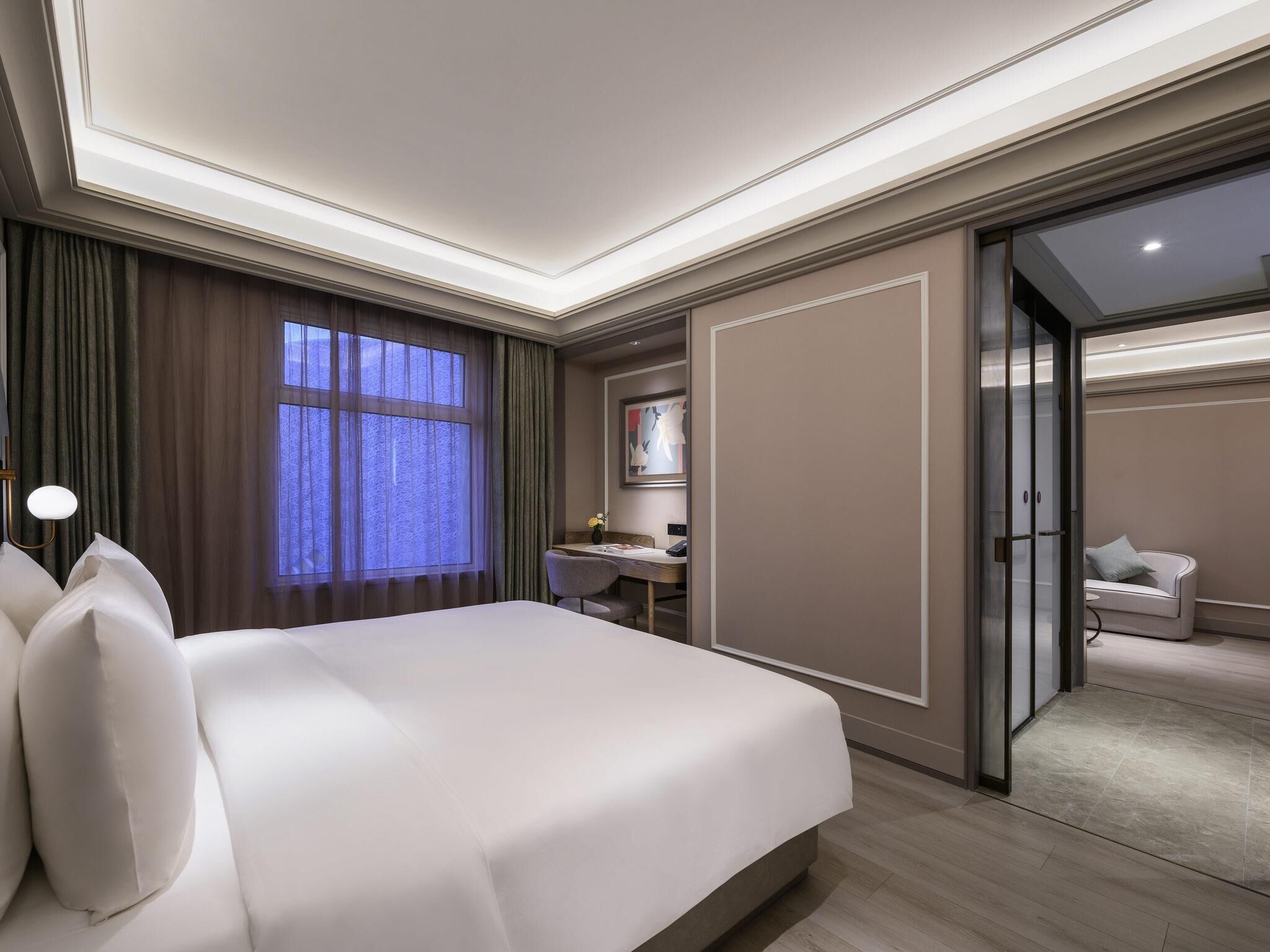Quarto de hotel com uma cama grande, uma escrivaninha, uma cadeira, uma mesa pequena e uma porta deslizante que dá para uma varanda.