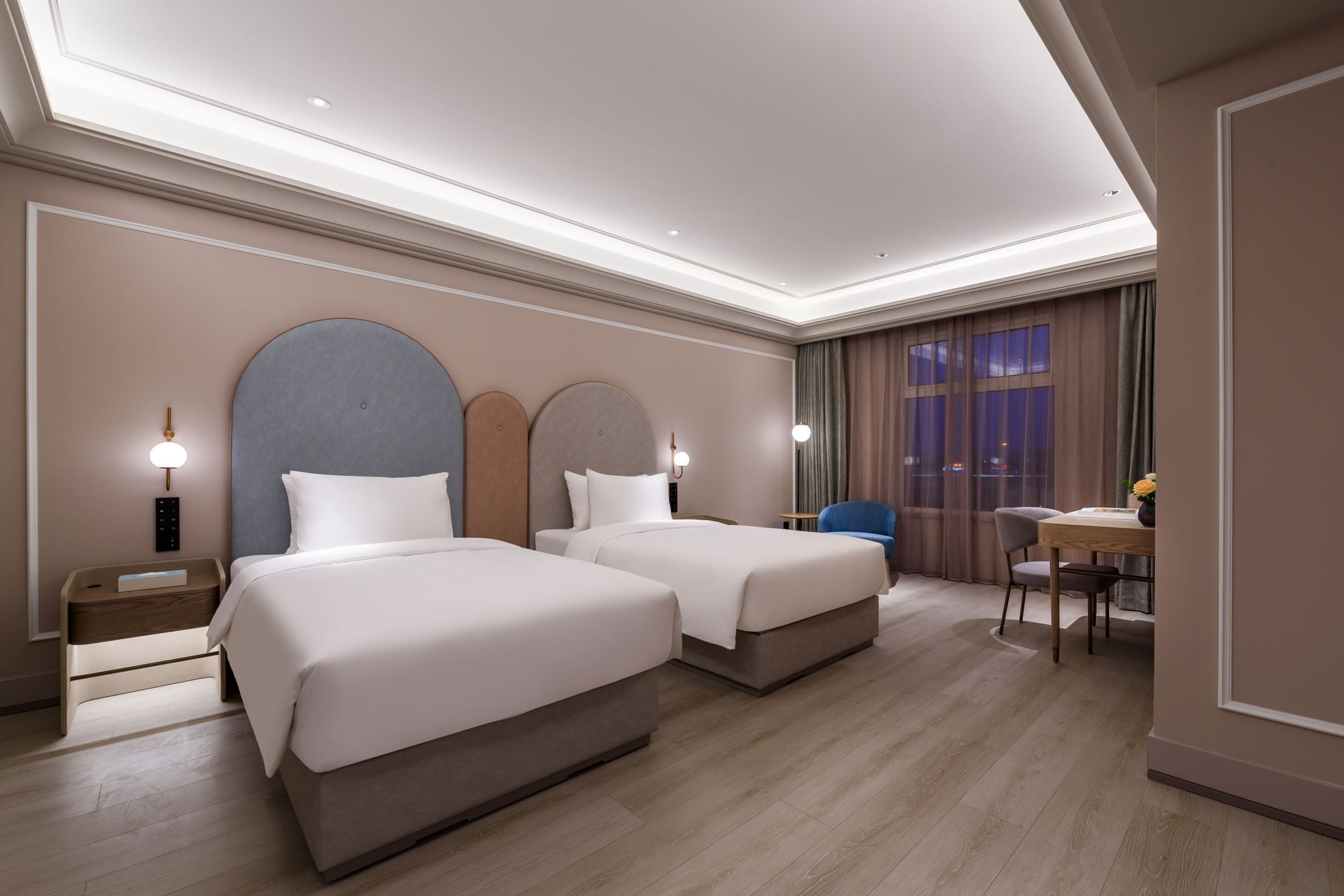 A hotel room with two beds, a desk, a chair, and a window with curtains.