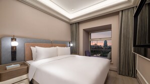 Une chambre d’hôtel moderne avec un grand lit, une table de chevet, une télévision et une fenêtre donnant sur la ville.