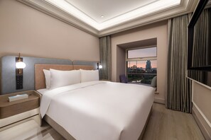 Een moderne hotelkamer met een groot bed, een nachtkastje, een televisie en een raam met uitzicht op de stad.