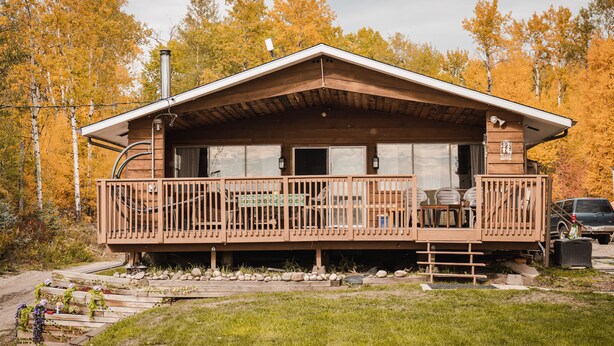 A cabin with a wooden deck, large windows, and a covered porch.