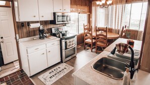 A kitchen with white cabinets, a microwave, an oven, a sink, and a dining area with wooden chairs and a table.