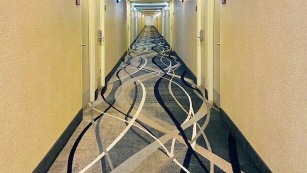 Un couloir d’hôtel avec un tapis à motifs, des appliques murales et des portes.