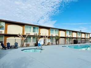 A motel with a swimming pool, outdoor seating, and a fenced area.