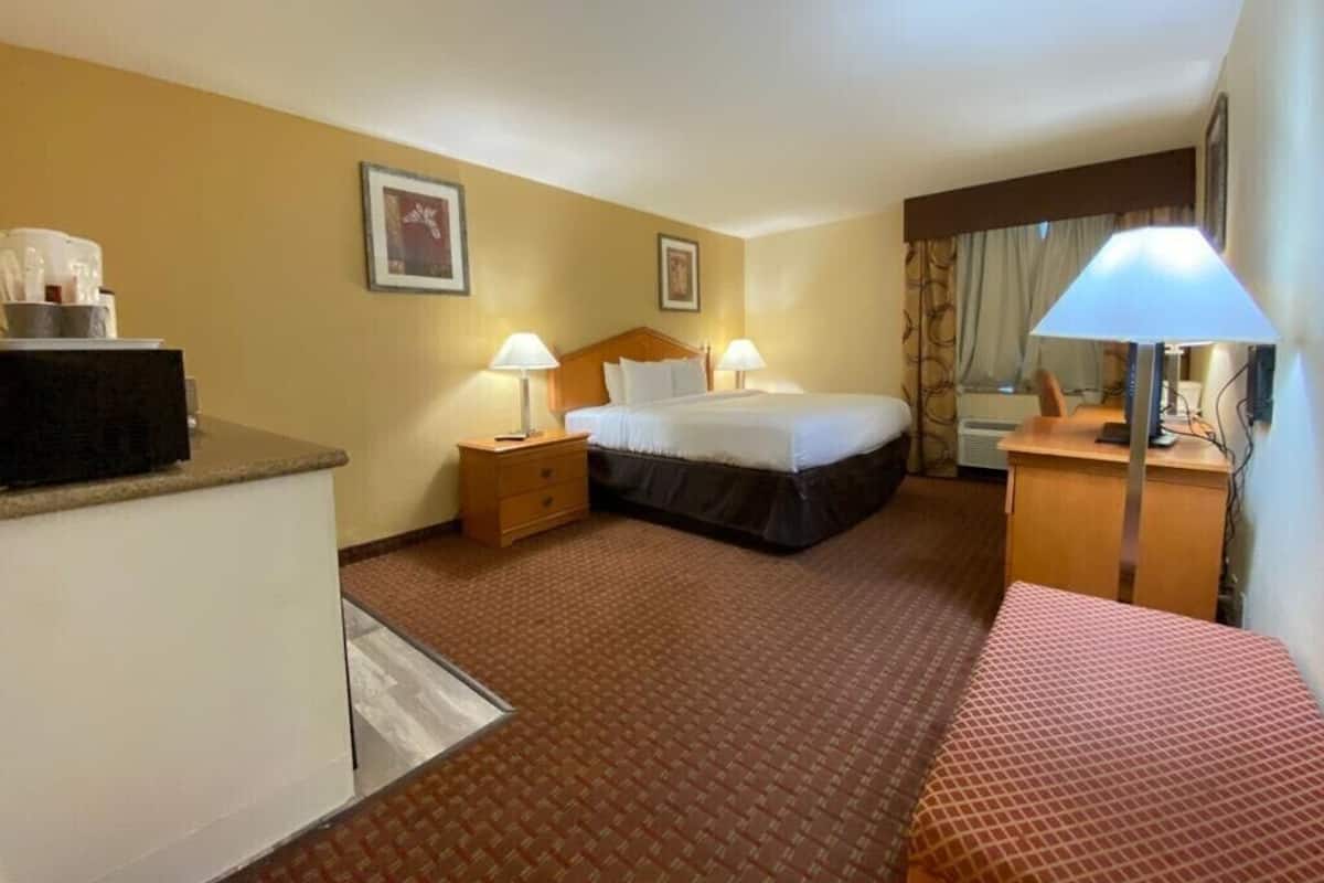 A hotel room with a bed, bedside tables, lamps, a desk, and a chair.