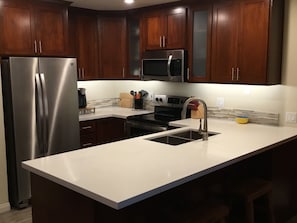 Une cuisine moderne avec des meubles en bois foncé, des appareils en acier inoxydable, un plan de travail blanc et un évier encastré.
