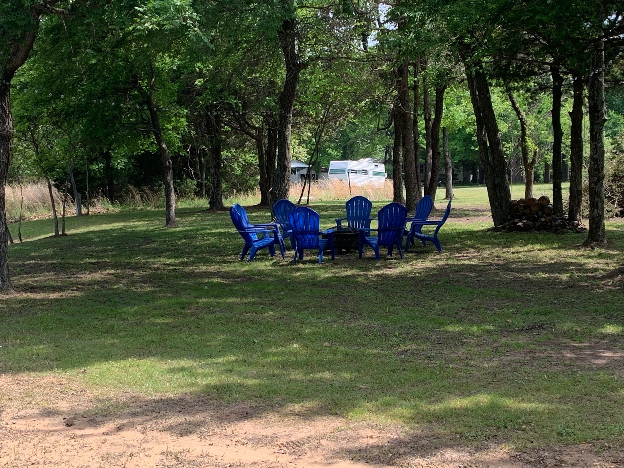 A campsite with blue chairs and a table under trees.