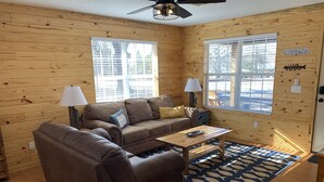 A cozy cabin interior with a brown leather sofa, a wooden coffee table, and a fish-patterned rug.