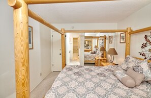 A bedroom with a wooden four-poster bed, a large mirror, and a bedside table with lamps.