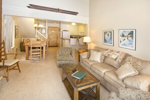 A living room with a wooden coffee table, a beige sofa, patterned armchairs, and a dining area with a wooden table and chairs. - St Anton Condos #58 (2-Bedroom) with Pool by RedAwning (Mammoth Lakes)