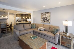 A modern living room with a sectional sofa, a coffee table, and a kitchen in the background.