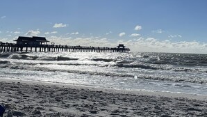 Een strand met een pier die zich uitstrekt over de oceaan, met een redershutje en een overdekt zitgedeelte.