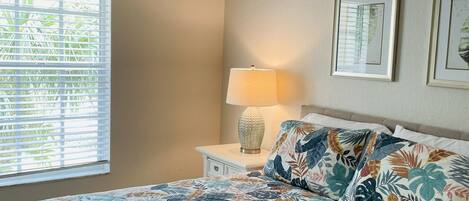 A bedroom with a bed, a nightstand, a lamp, and a window with blinds.