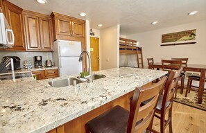 A kitchen with wooden cabinets, a granite countertop, a stainless steel sink, and a built-in bench.