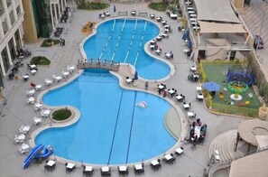 A large outdoor swimming pool with multiple lanes, surrounded by outdoor seating areas and a children's play area.