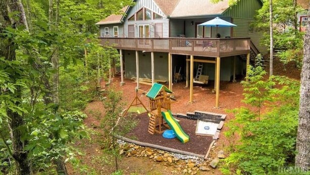 Une maison à deux étages avec une terrasse, entourée d’une forêt dense.