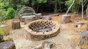 Un foyer circulaire entouré d’escaliers en pierre, avec un banc en bois et une table en bois rustique à proximité.