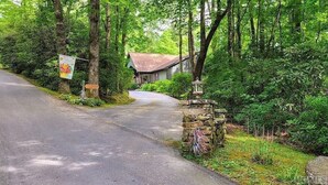 Un chemin de campagne menant à une maison entourée d’une forêt dense.