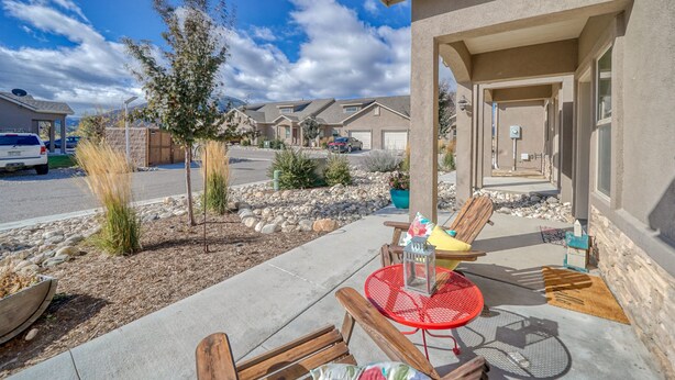 A residential area with a patio featuring wooden chairs and a red metal table, surrounded by a landscaped garden with rocks and plants. - Beautiful Town Home in Poncha Springs- minutes to Monarch Mountain (Poncha Springs)