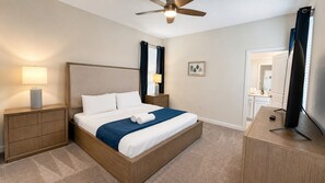 Une chambre d’hôtel avec un lit, des tables de chevet, un ventilateur de plafond, une télévision et une salle de bain visible à travers une porte ouverte.